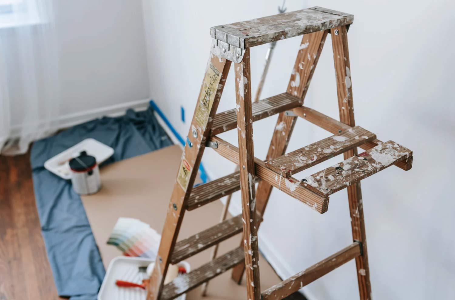 clean-2 A paint-splattered wooden ladder stands by a wall with painting supplies and color swatches nearby.