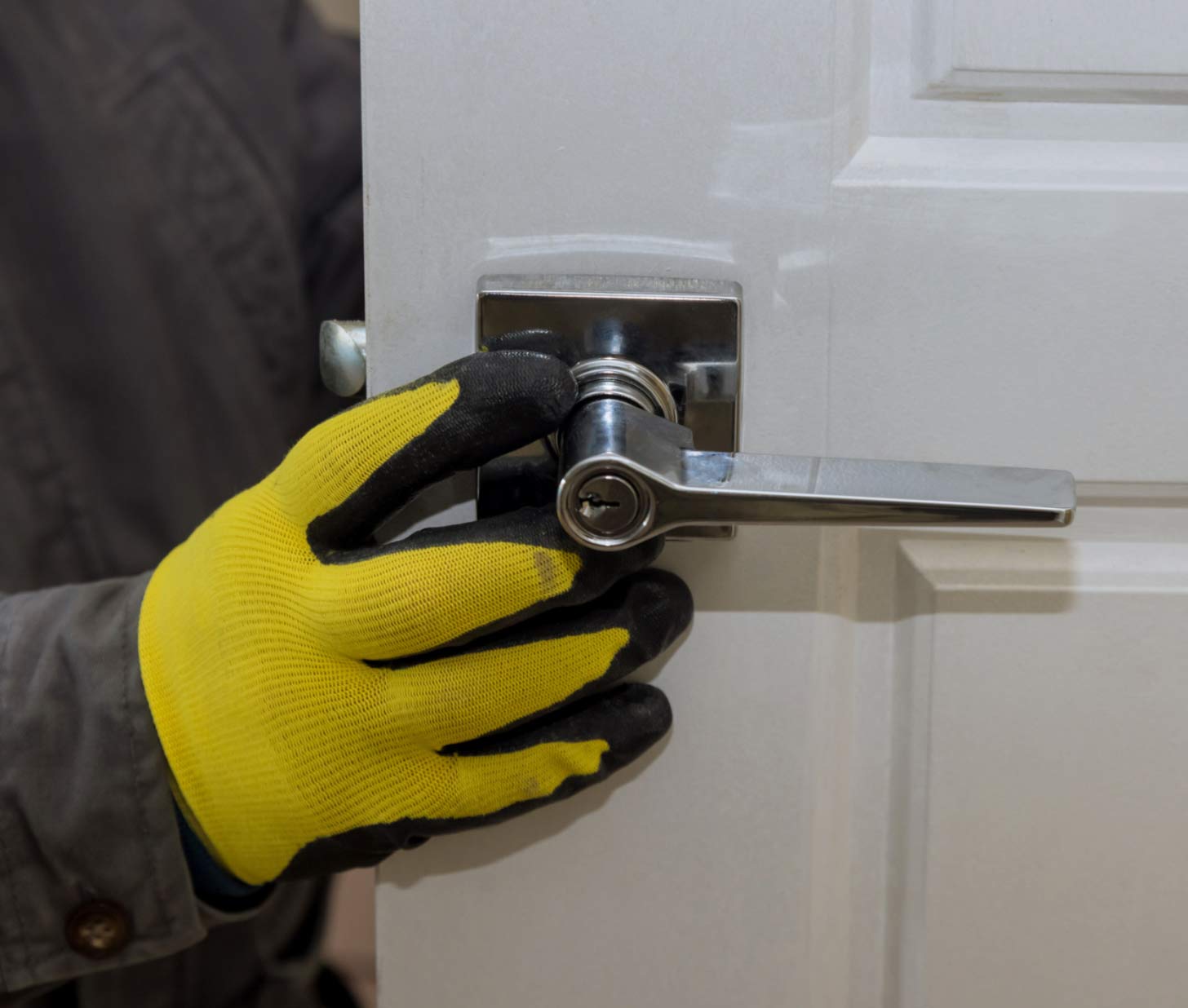 door-3 Person wearing yellow gloves installing or fixing a silver door handle on a white door.
