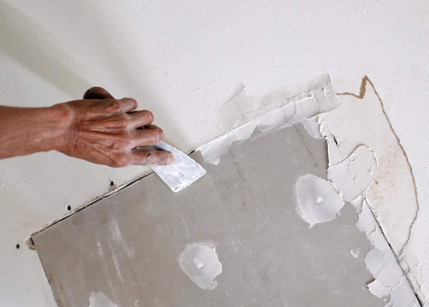drywall-3 A hand uses a putty knife to spread plaster over drywall for a wall repair.