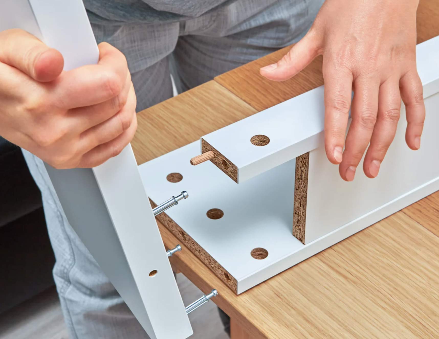 furniture-2 Close-up of hands assembling wooden furniture with screws and dowels on a wooden surface.