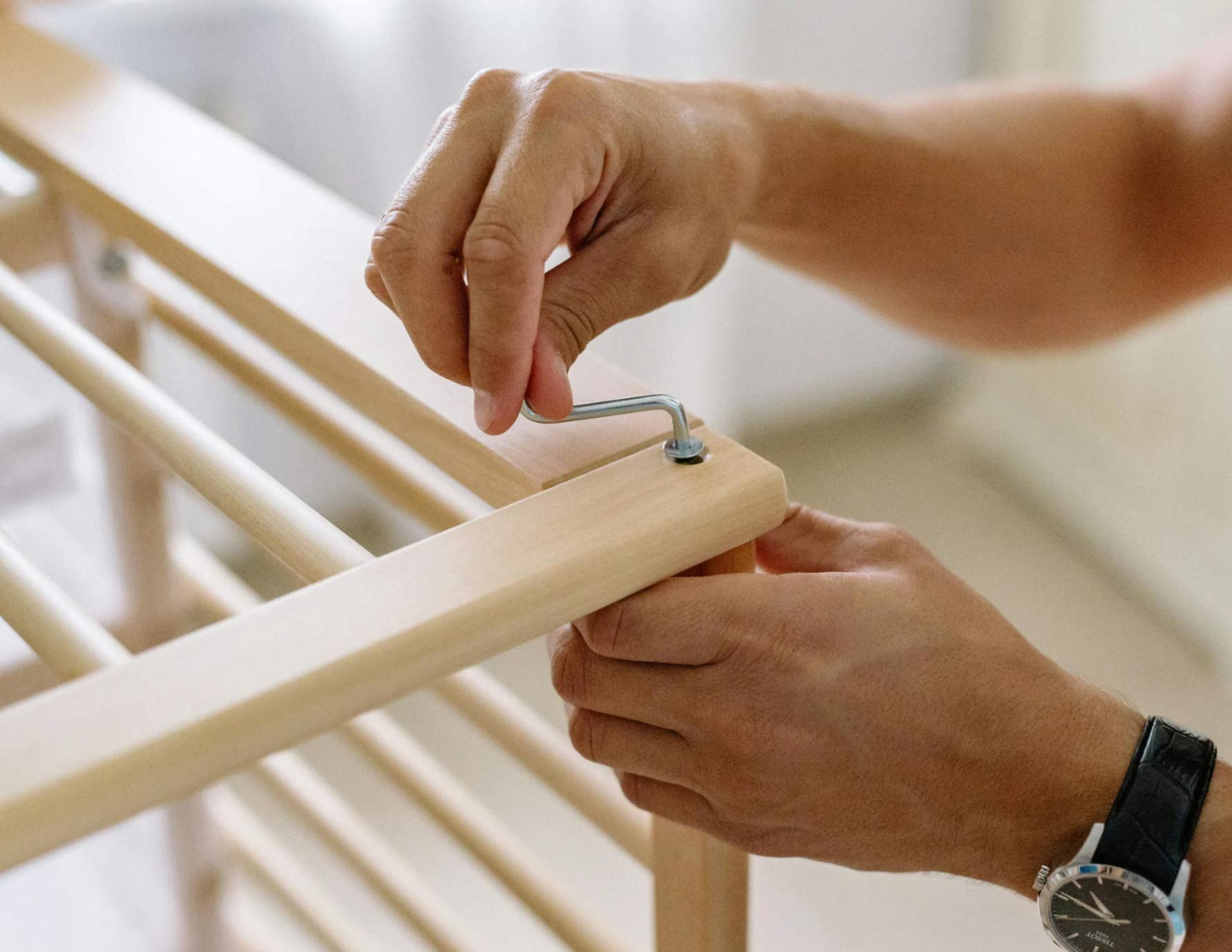 furniture-3 Person assembling wooden furniture with an Allen wrench, tightening a bolt on a light wood frame.