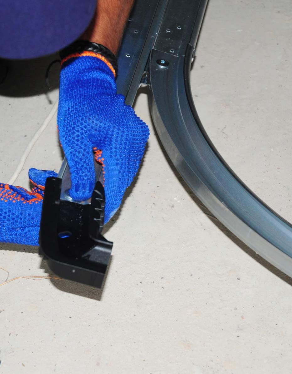 garafe-2 Person wearing blue gloves installing or adjusting a metal track on a concrete floor.