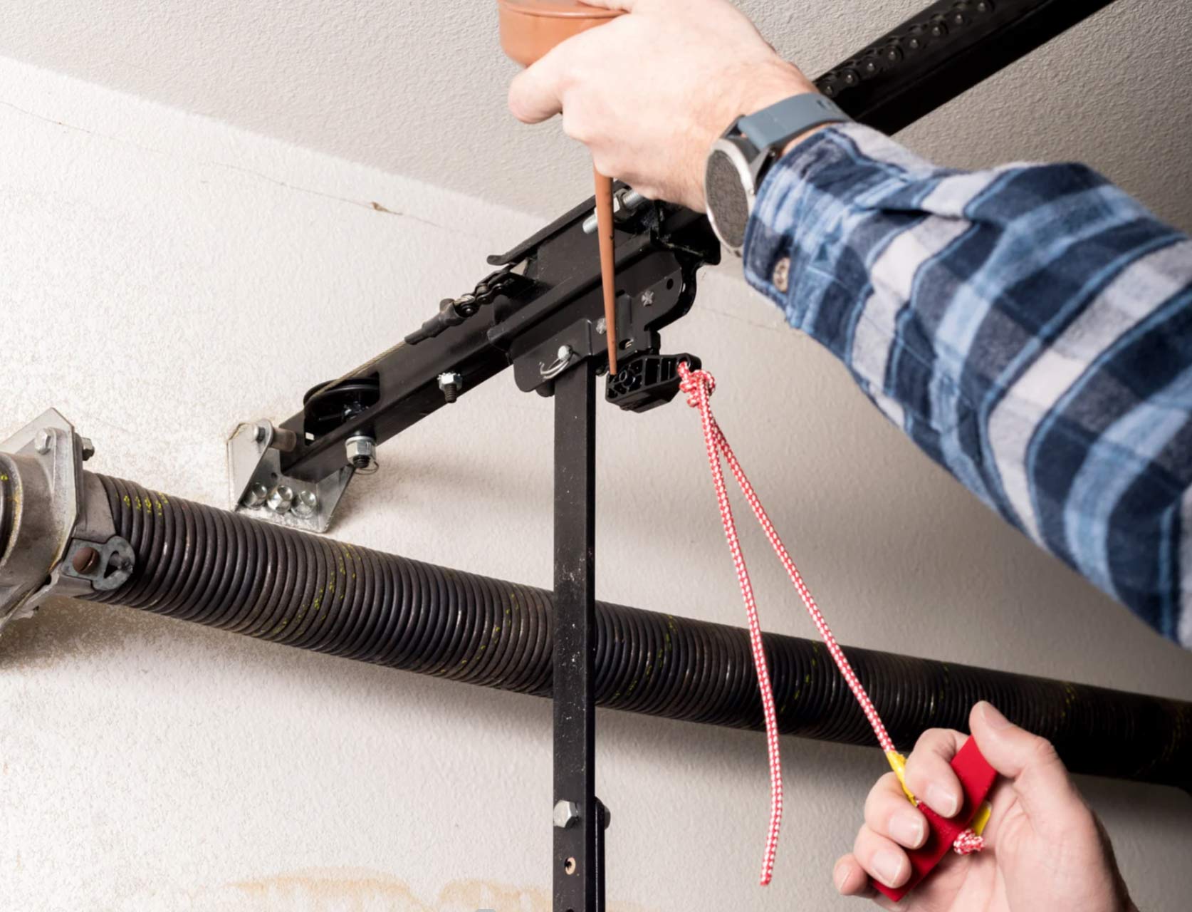 garage-1 Person lubricating a garage door opener mechanism with one hand while holding a red cord with the other.