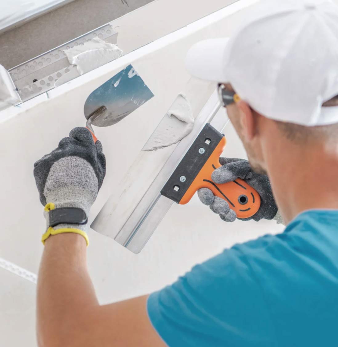 sheet-img A person applies plaster to a wall using a trowel and a putty knife, wearing gloves and a cap.