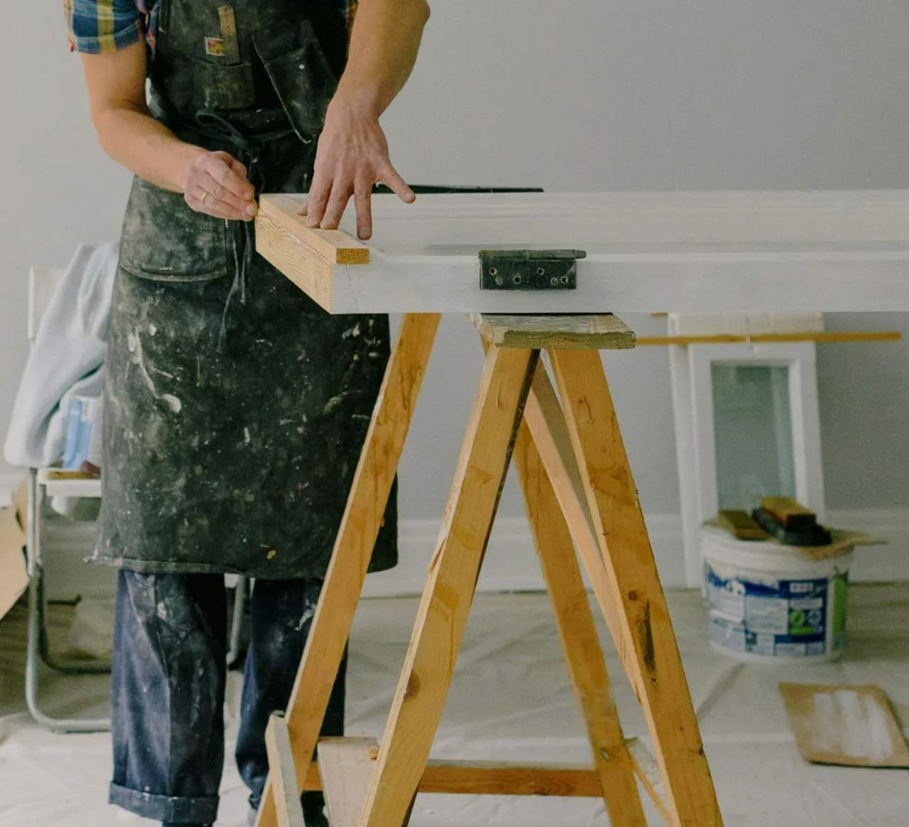 special-1 Person in overalls working on a door placed on a sawhorse in a room under renovation.