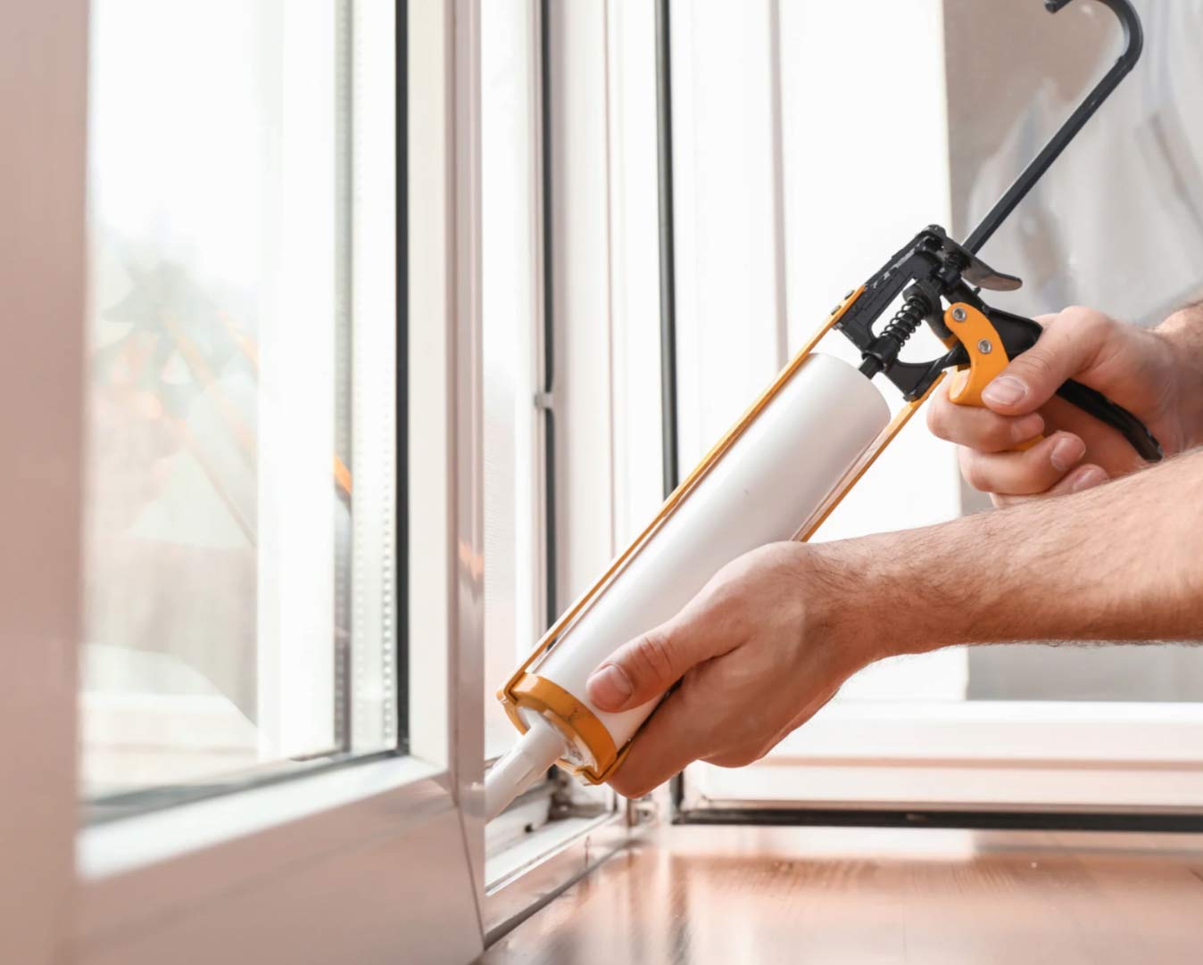 special-2 Hands sealing a window frame with a caulking gun, applying white sealant along the edge.