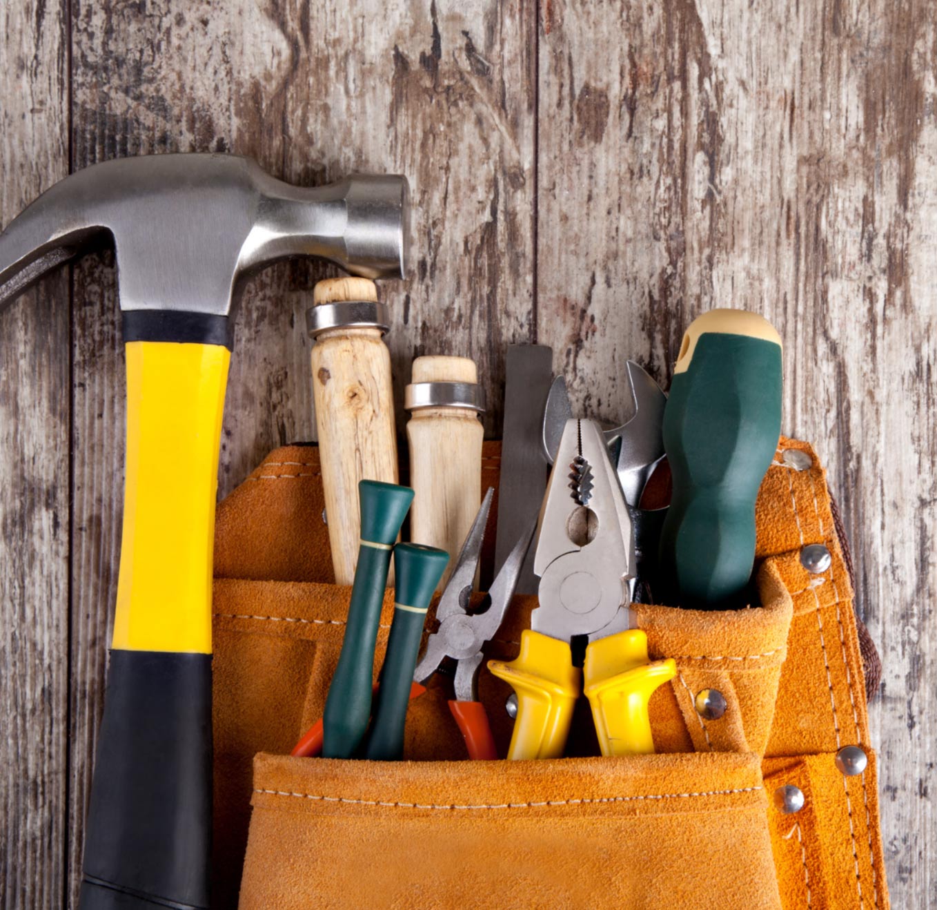 tools-img Brown tool belt with a hammer, screwdrivers, pliers, and other tools against a rustic wooden background.