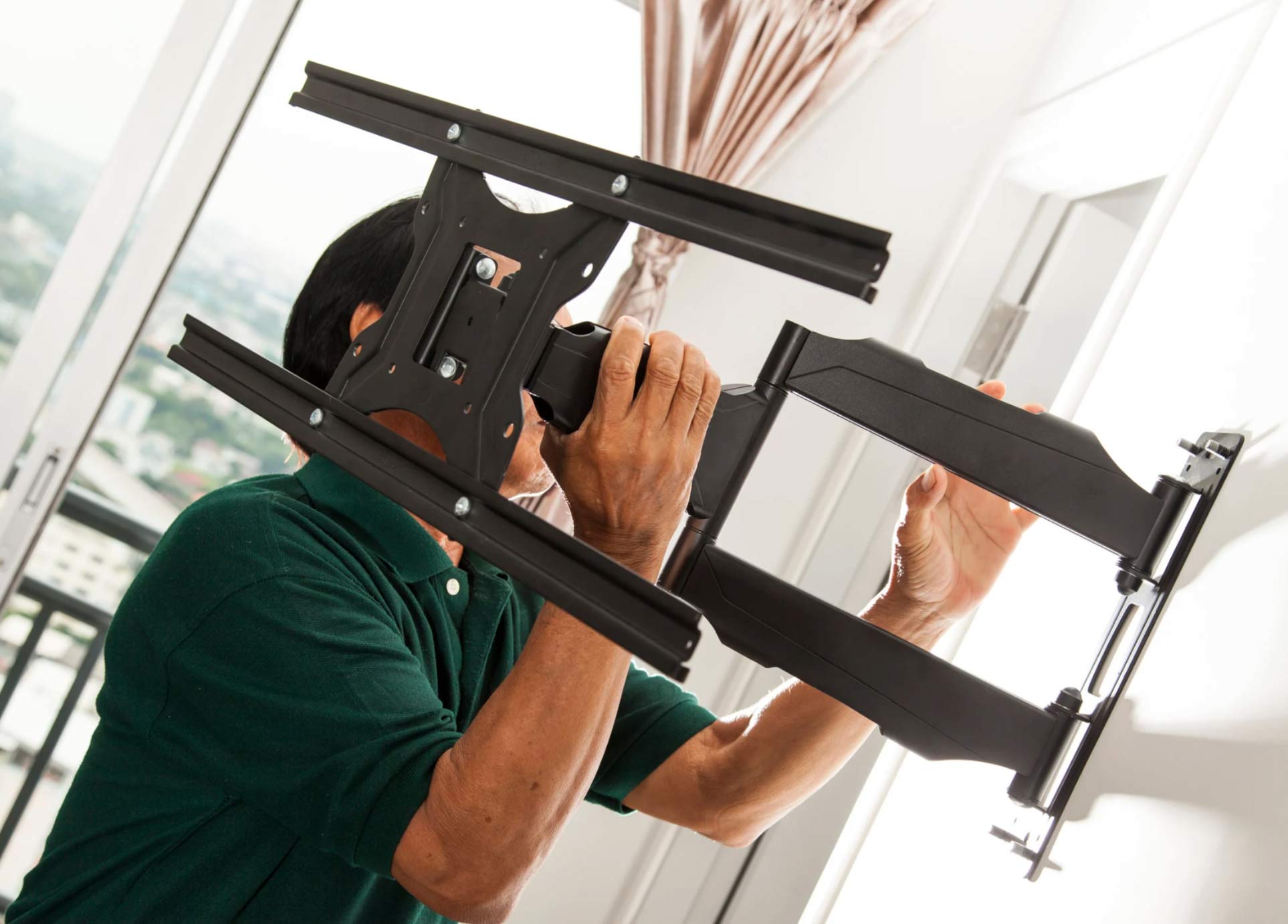 tv-2 Person installing a black TV wall mount bracket on a white wall near a window.